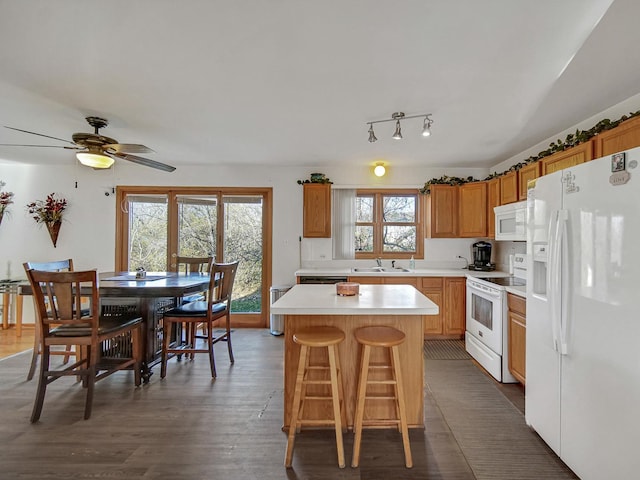 kitchen with ceiling fan, sink, white appliances, dark wood-type flooring, and a center island