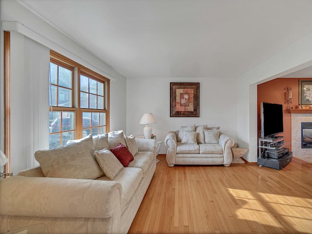 living room with a tiled fireplace and light wood-type flooring