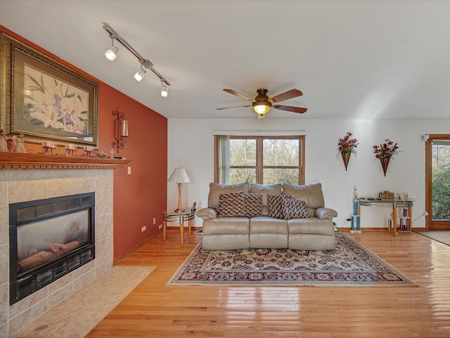 living room with ceiling fan, light wood-type flooring, a tile fireplace, and track lighting