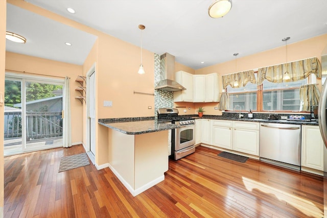 kitchen with stainless steel appliances, kitchen peninsula, wall chimney exhaust hood, and hanging light fixtures