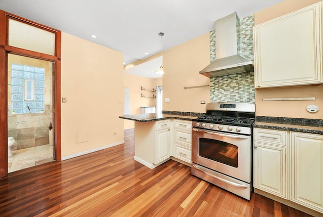 kitchen with hanging light fixtures, light wood-type flooring, kitchen peninsula, wall chimney range hood, and gas range