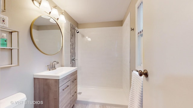 bathroom featuring a tile shower, vanity, and toilet