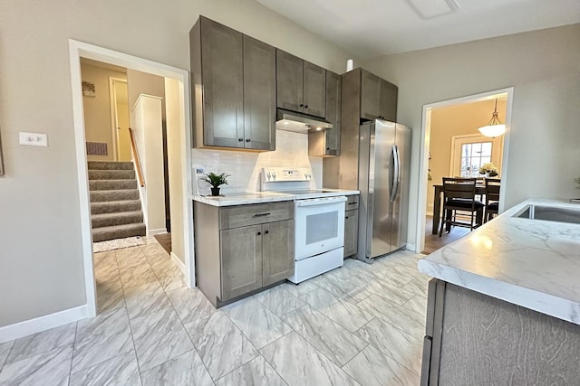 kitchen featuring white electric range oven, sink, stainless steel refrigerator, pendant lighting, and decorative backsplash