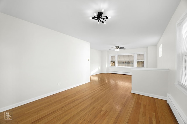 unfurnished living room with baseboard heating, wood-type flooring, and a healthy amount of sunlight