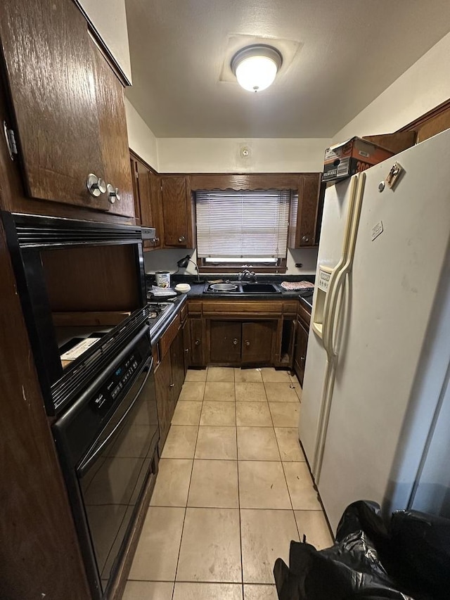 kitchen featuring black oven, light tile patterned flooring, dark brown cabinets, white fridge with ice dispenser, and sink