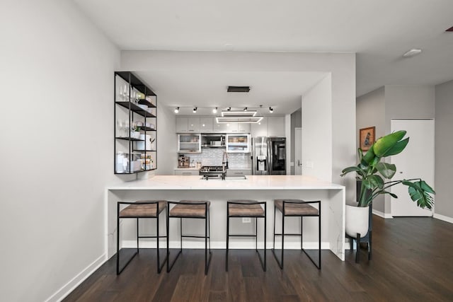 kitchen featuring a breakfast bar, dark hardwood / wood-style floors, tasteful backsplash, kitchen peninsula, and stainless steel appliances