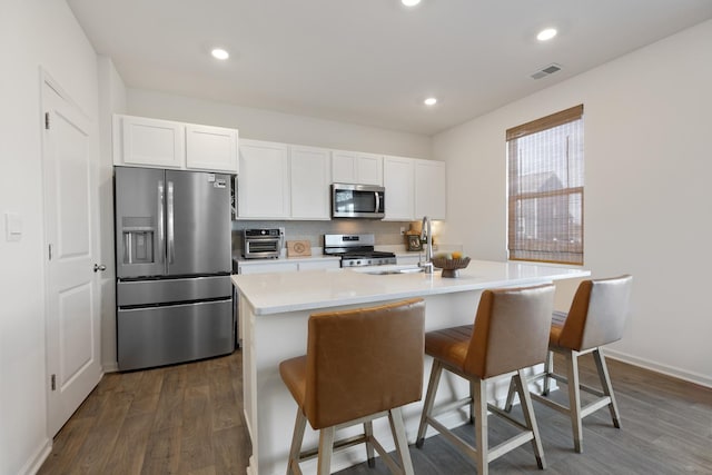 kitchen featuring dark wood-type flooring, white cabinetry, stainless steel appliances, a kitchen island with sink, and a breakfast bar area