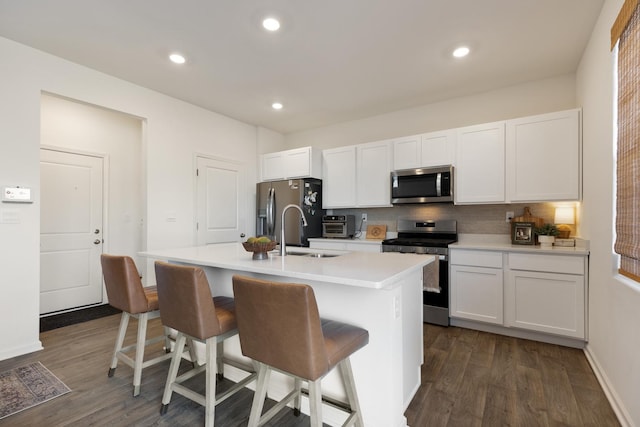 kitchen with white cabinetry, a kitchen island with sink, appliances with stainless steel finishes, a kitchen breakfast bar, and dark hardwood / wood-style flooring