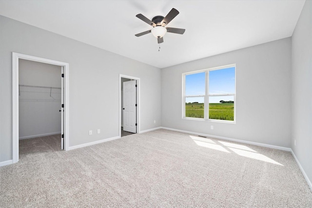 unfurnished bedroom featuring a walk in closet, light colored carpet, ceiling fan, and a closet