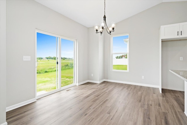 unfurnished dining area with a notable chandelier, plenty of natural light, lofted ceiling, and light hardwood / wood-style floors