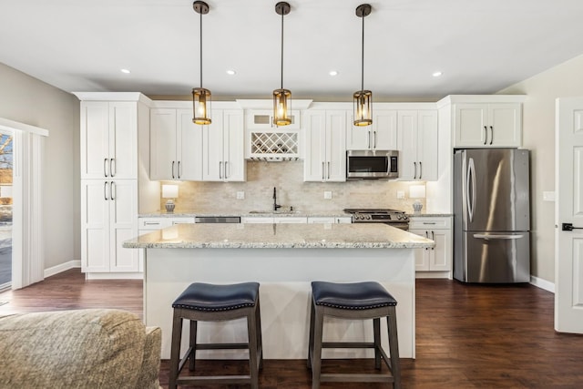 kitchen featuring pendant lighting, sink, light stone countertops, stainless steel appliances, and white cabinets