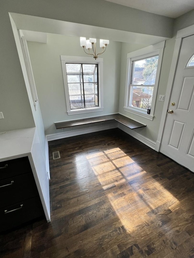 unfurnished dining area featuring a healthy amount of sunlight, a notable chandelier, and dark hardwood / wood-style floors