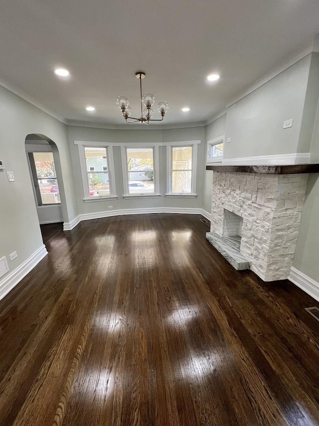 unfurnished living room with a notable chandelier, hardwood / wood-style floors, a stone fireplace, and ornamental molding