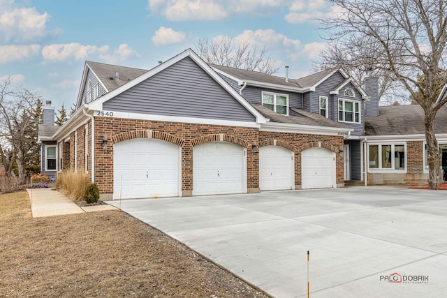 view of front of property featuring an attached garage, brick siding, a shingled roof, driveway, and a chimney