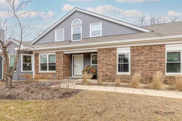 view of front of home with a shingled roof, brick siding, and a porch