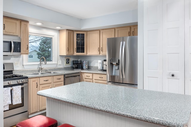 kitchen featuring a breakfast bar area, appliances with stainless steel finishes, light stone counters, light brown cabinets, and sink