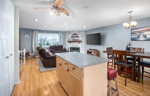 kitchen with a center island, a brick fireplace, light brown cabinetry, light hardwood / wood-style flooring, and ceiling fan with notable chandelier