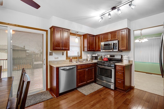 kitchen featuring dark wood-type flooring, sink, pendant lighting, stainless steel appliances, and ceiling fan with notable chandelier