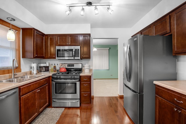 kitchen with sink, decorative light fixtures, stainless steel appliances, and light wood-type flooring