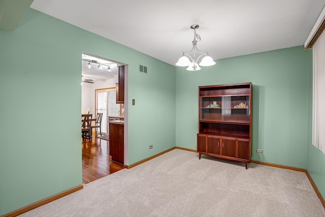 unfurnished room with a notable chandelier, light colored carpet, and rail lighting