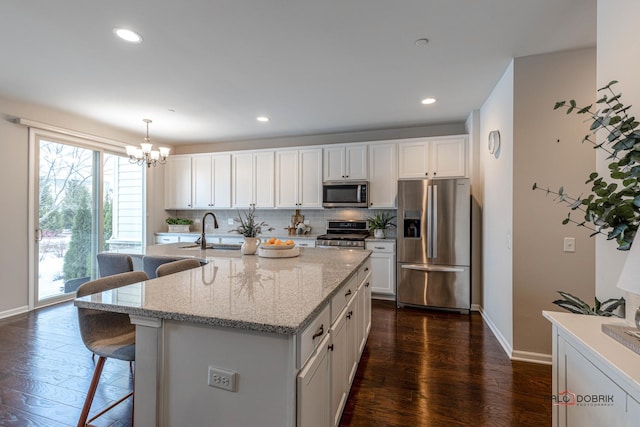 kitchen featuring stainless steel appliances, pendant lighting, white cabinets, and a kitchen island with sink