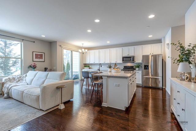 kitchen featuring decorative light fixtures, a kitchen island, white cabinetry, stainless steel appliances, and dark hardwood / wood-style flooring