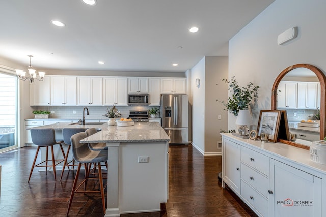 kitchen with decorative light fixtures, a kitchen island with sink, stainless steel appliances, white cabinets, and dark hardwood / wood-style flooring