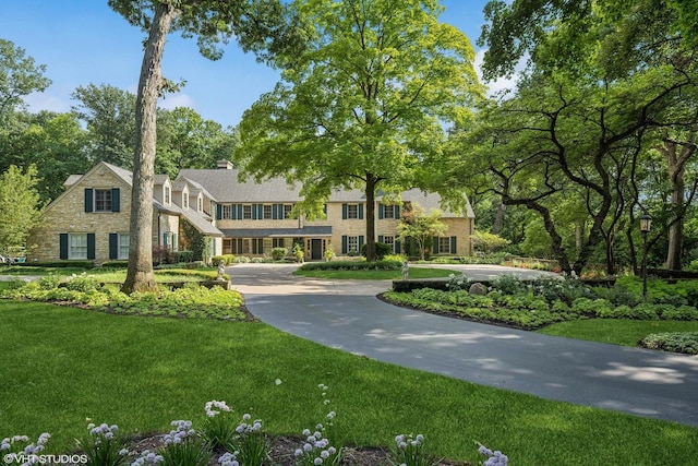 view of front of home featuring driveway, a front lawn, and a chimney