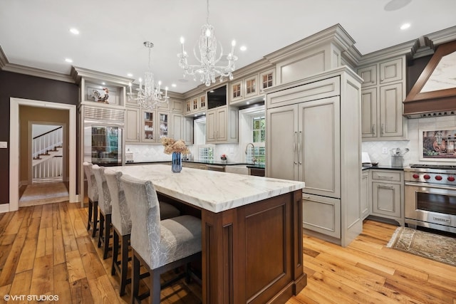 kitchen featuring premium appliances, custom exhaust hood, ornamental molding, a kitchen island, and light stone countertops