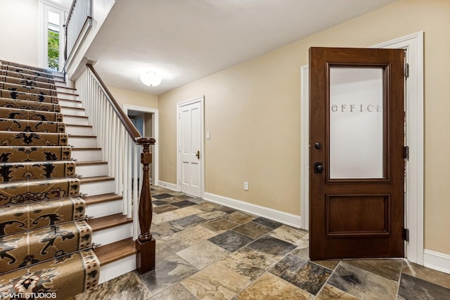 foyer entrance with baseboards, stone tile floors, and stairs