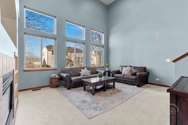 carpeted living room featuring a tiled fireplace and a towering ceiling