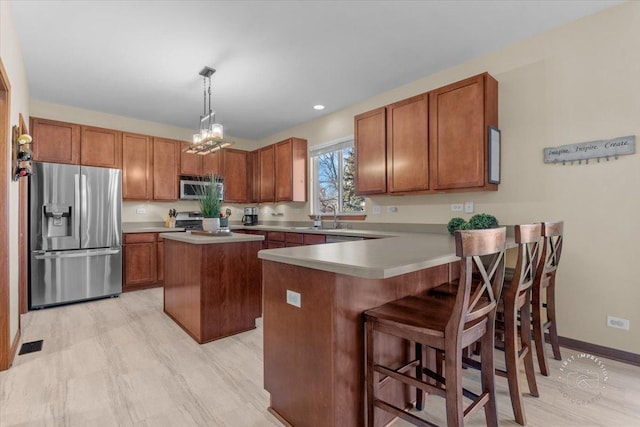 kitchen featuring a kitchen island, appliances with stainless steel finishes, decorative light fixtures, sink, and a kitchen bar