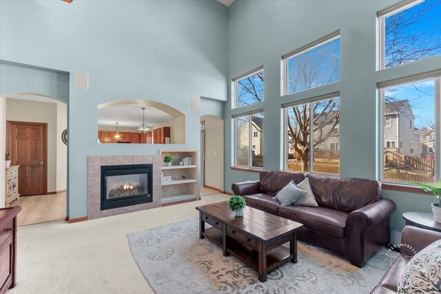 carpeted living room featuring a tiled fireplace, plenty of natural light, and a towering ceiling