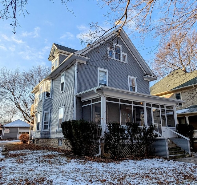 snow covered back of property with a sunroom