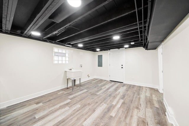 basement featuring light wood-type flooring, sink, and electric panel