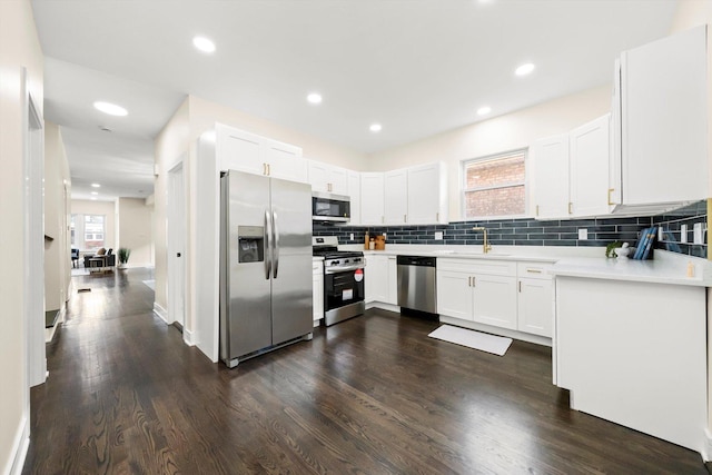 kitchen featuring appliances with stainless steel finishes, dark hardwood / wood-style floors, backsplash, white cabinets, and sink