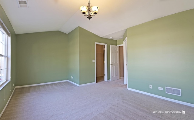 empty room featuring vaulted ceiling, a chandelier, and light colored carpet