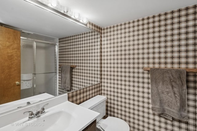 bathroom featuring toilet, vanity, and a shower with shower door