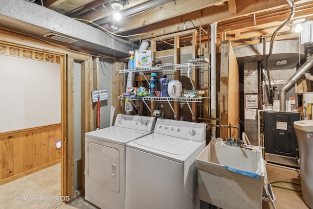 laundry area featuring wooden walls, heating unit, separate washer and dryer, light carpet, and sink