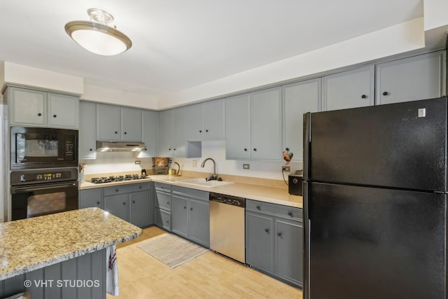 kitchen featuring light stone countertops, black appliances, light wood-type flooring, gray cabinets, and sink