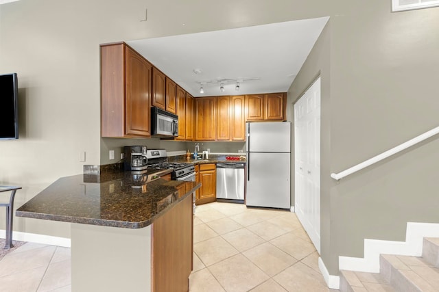 kitchen featuring kitchen peninsula, track lighting, light tile patterned floors, dark stone counters, and appliances with stainless steel finishes