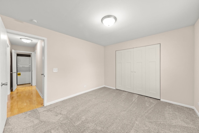 unfurnished bedroom featuring stacked washer and clothes dryer, a closet, and light carpet