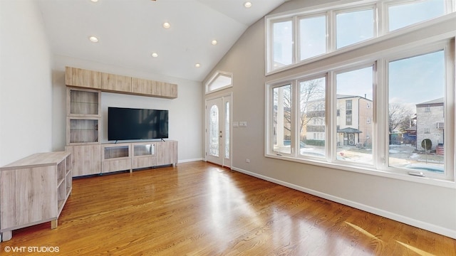 unfurnished living room featuring high vaulted ceiling, a healthy amount of sunlight, and hardwood / wood-style flooring