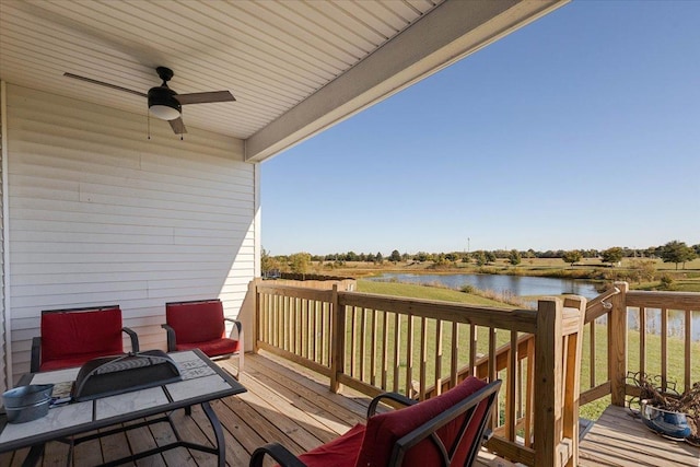 wooden deck featuring ceiling fan, a water view, and a lawn