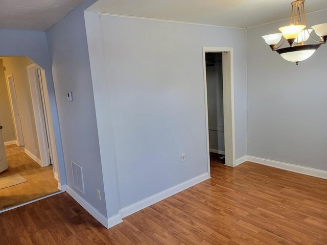 empty room featuring wood-type flooring and a chandelier