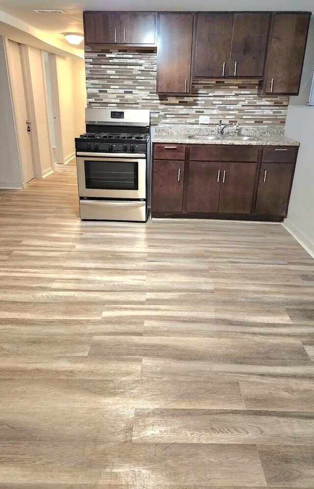 kitchen with light wood-type flooring, dark brown cabinets, stainless steel gas stove, light stone countertops, and sink