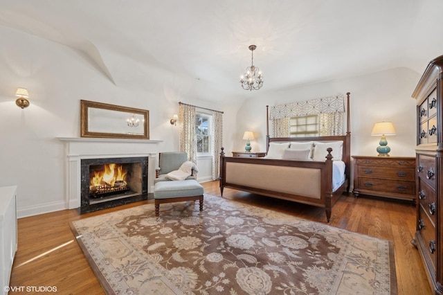 bedroom with a chandelier, hardwood / wood-style floors, a premium fireplace, and vaulted ceiling