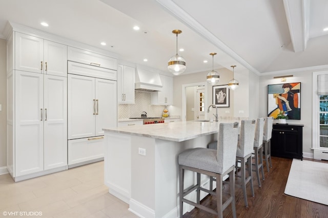 kitchen featuring light stone countertops, pendant lighting, custom exhaust hood, white cabinetry, and sink