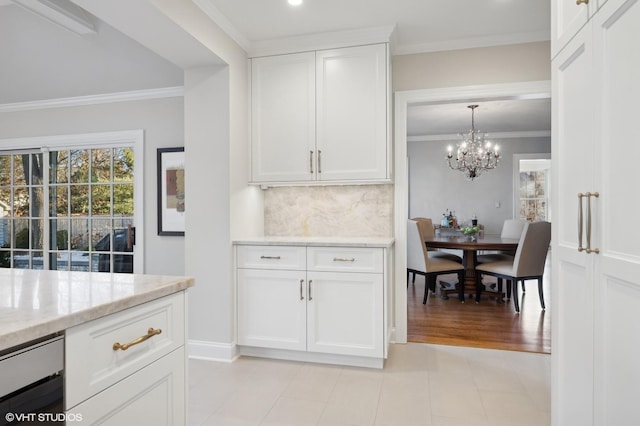 kitchen with backsplash, white cabinetry, light stone countertops, ornamental molding, and a chandelier