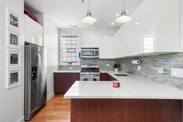 kitchen featuring decorative light fixtures, kitchen peninsula, sink, stainless steel appliances, and white cabinets